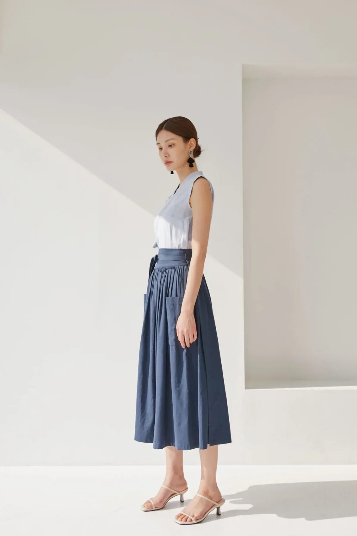 Woman wearing navy blue midi skirt with pockets and sleeveless white top in bright studio