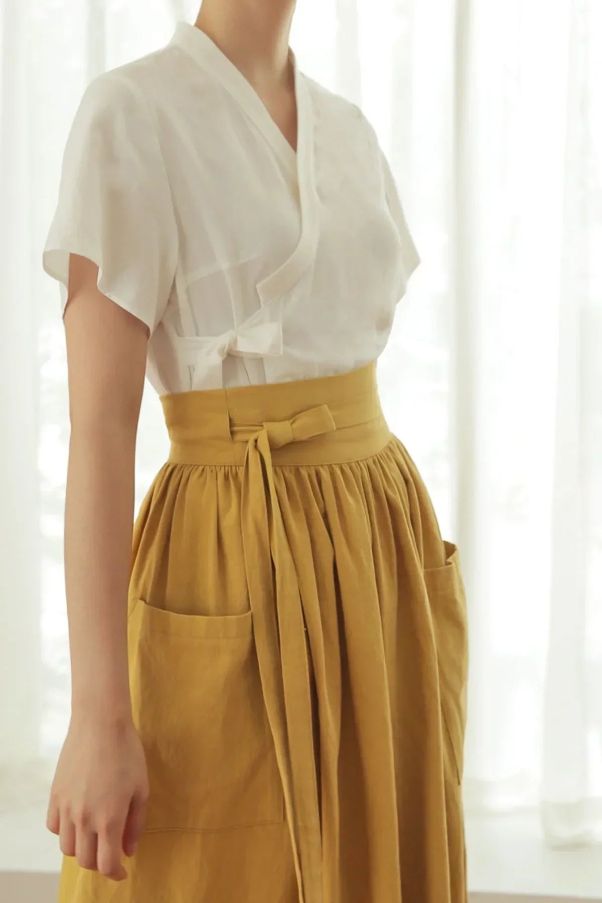 Close-up of a woman wearing a white wrap blouse and mustard high-waisted skirt with pockets and tied belt