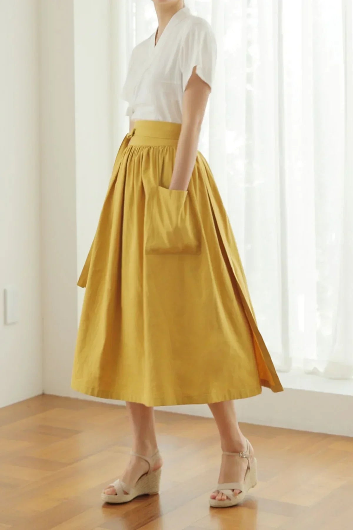 Woman wearing mustard yellow midi skirt with side pocket and white short-sleeve top in bright room