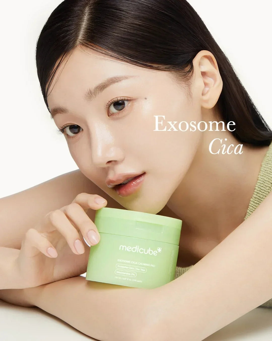 Woman with clear skin holding green Medicube Exosome Cica Calming Pad container