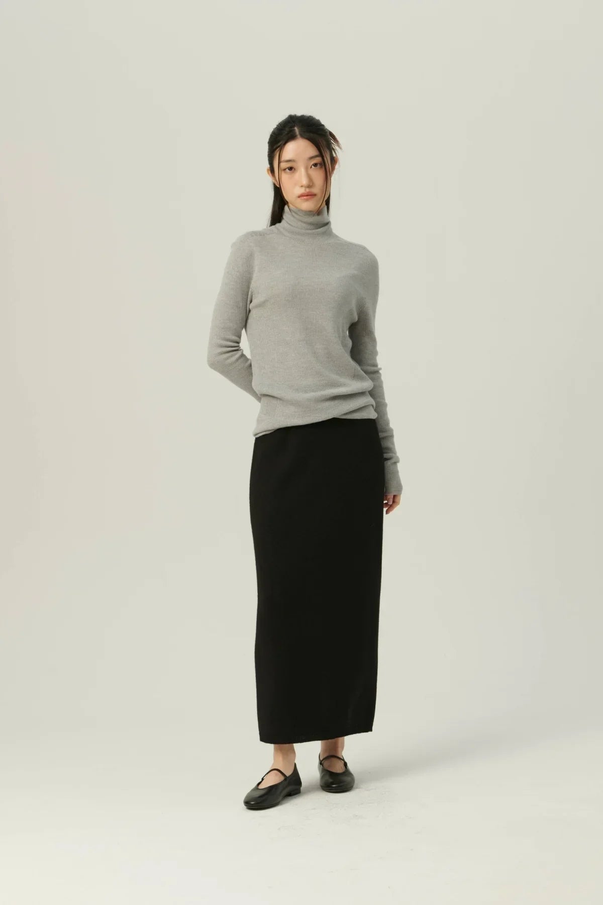 Woman wearing gray fine rib wool turtleneck sweater with long black skirt and black flats
