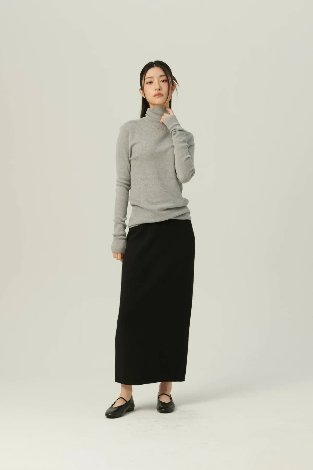 Woman wearing gray fine rib wool turtleneck and long black skirt in minimalist studio