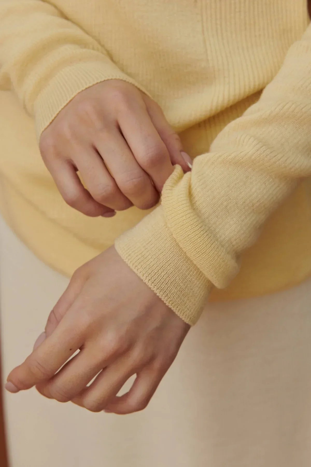 Close-up of hands adjusting yellow fine rib wool sweater sleeves