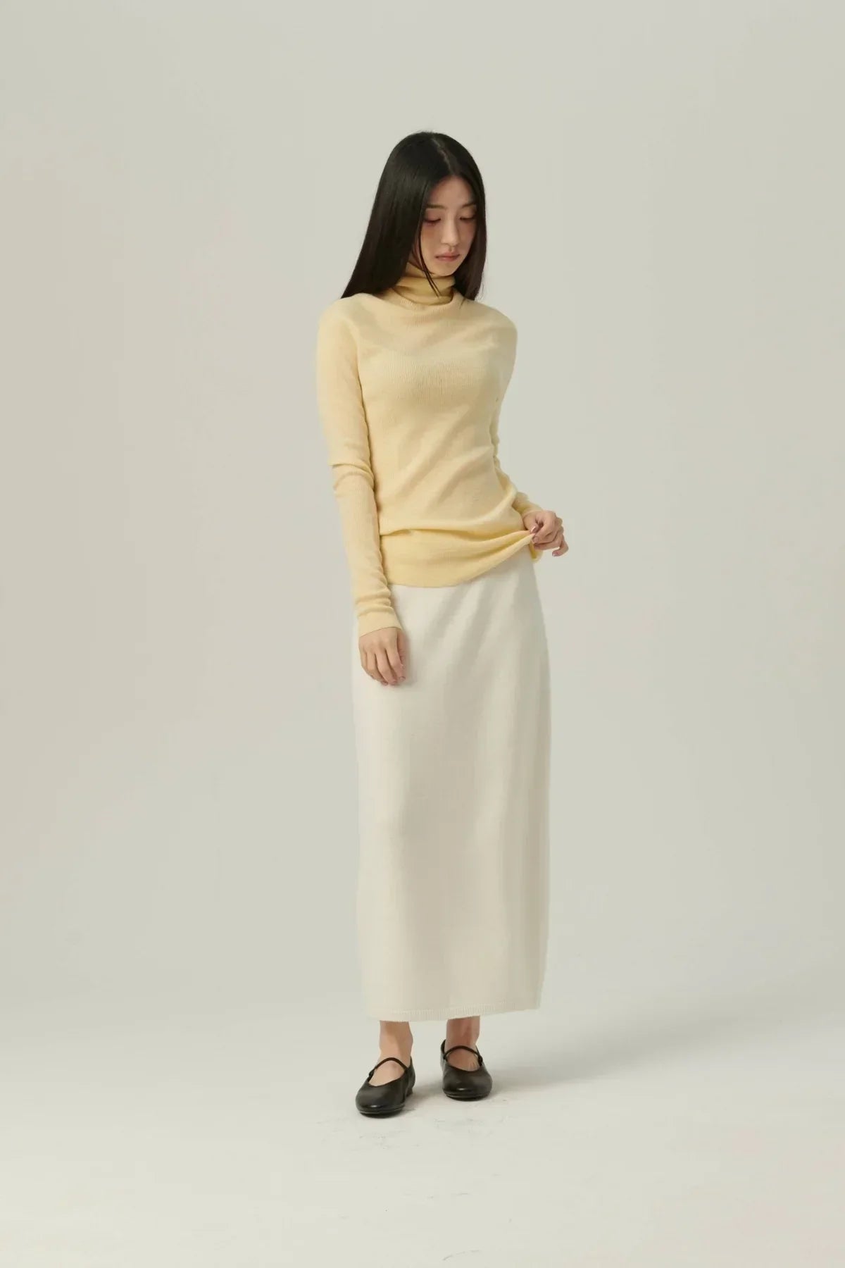Asian woman wearing a yellow fine rib wool turtleneck sweater and a white long skirt with black shoes
