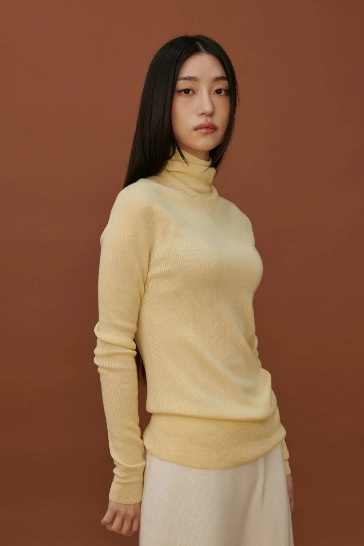 Asian woman wearing fine rib yellow wool turtleneck sweater against brown background
