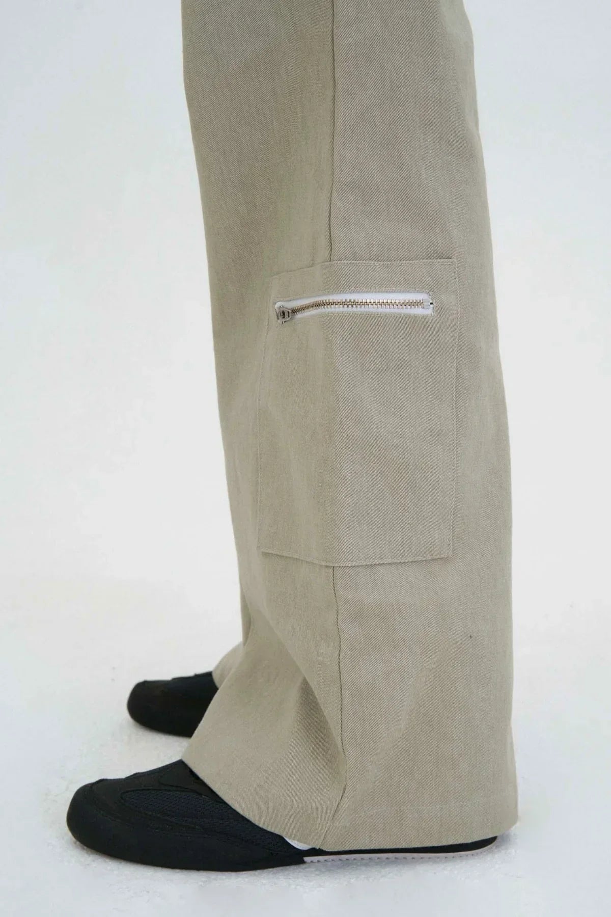 Beige flared cargo pants with zippered pocket detail on side, paired with black shoes