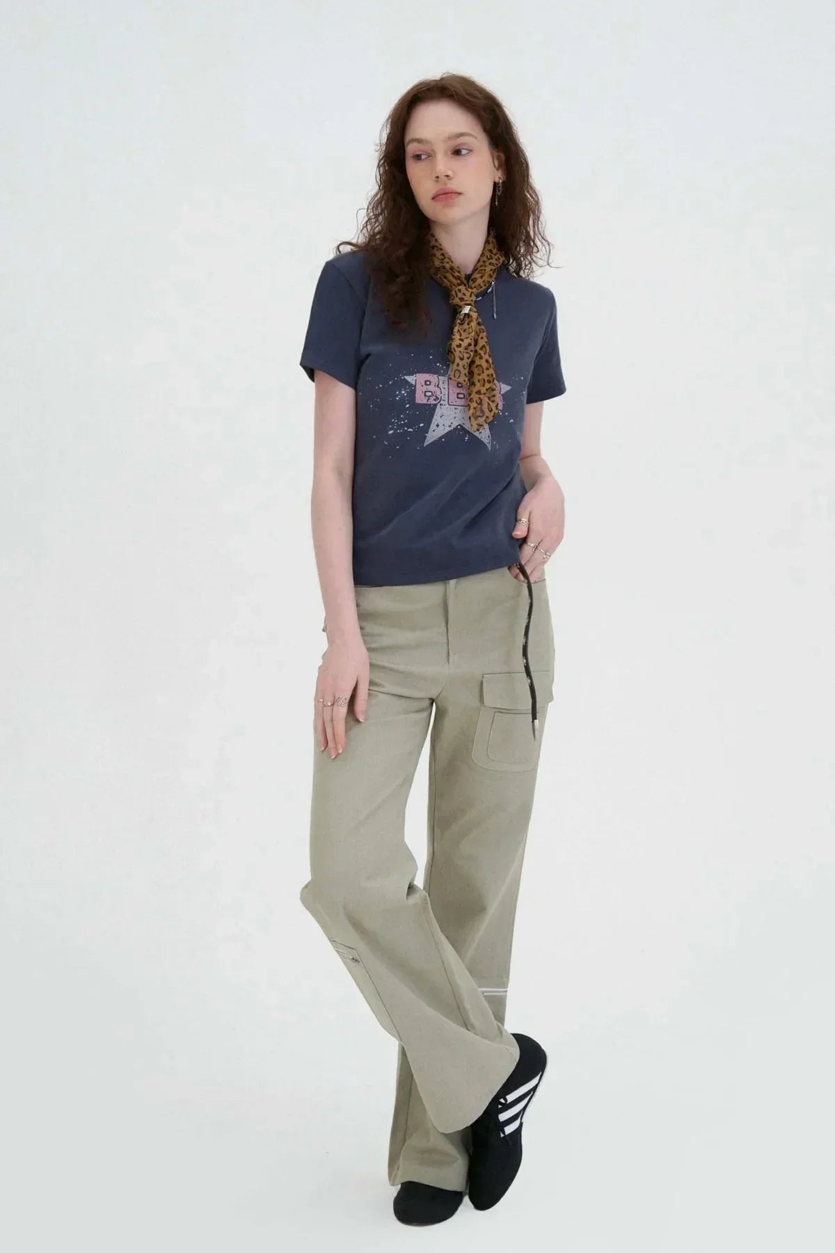 woman wearing beige flared cargo pants, navy graphic t-shirt, leopard print scarf, and black sneakers