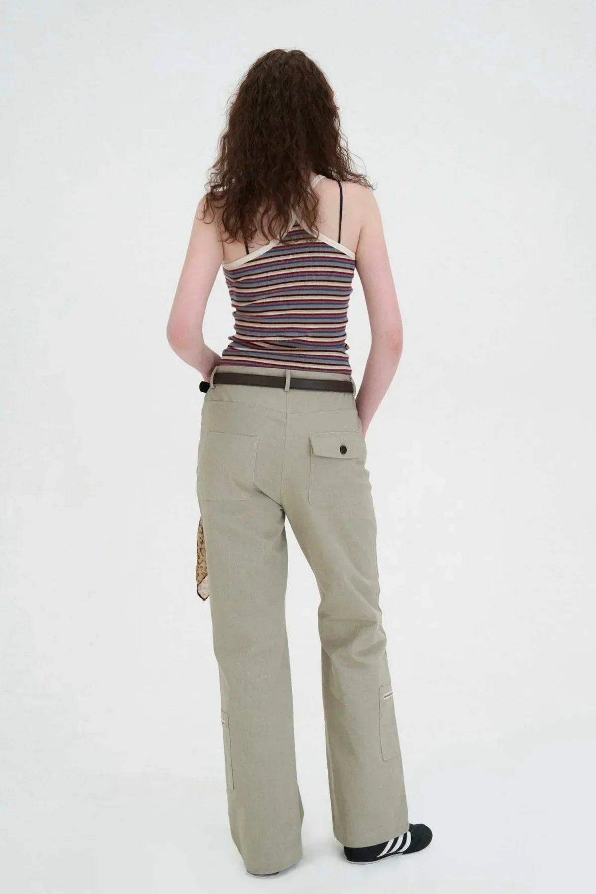 Woman wearing beige flared cargo pants with back pockets and a striped sleeveless top in a white studio