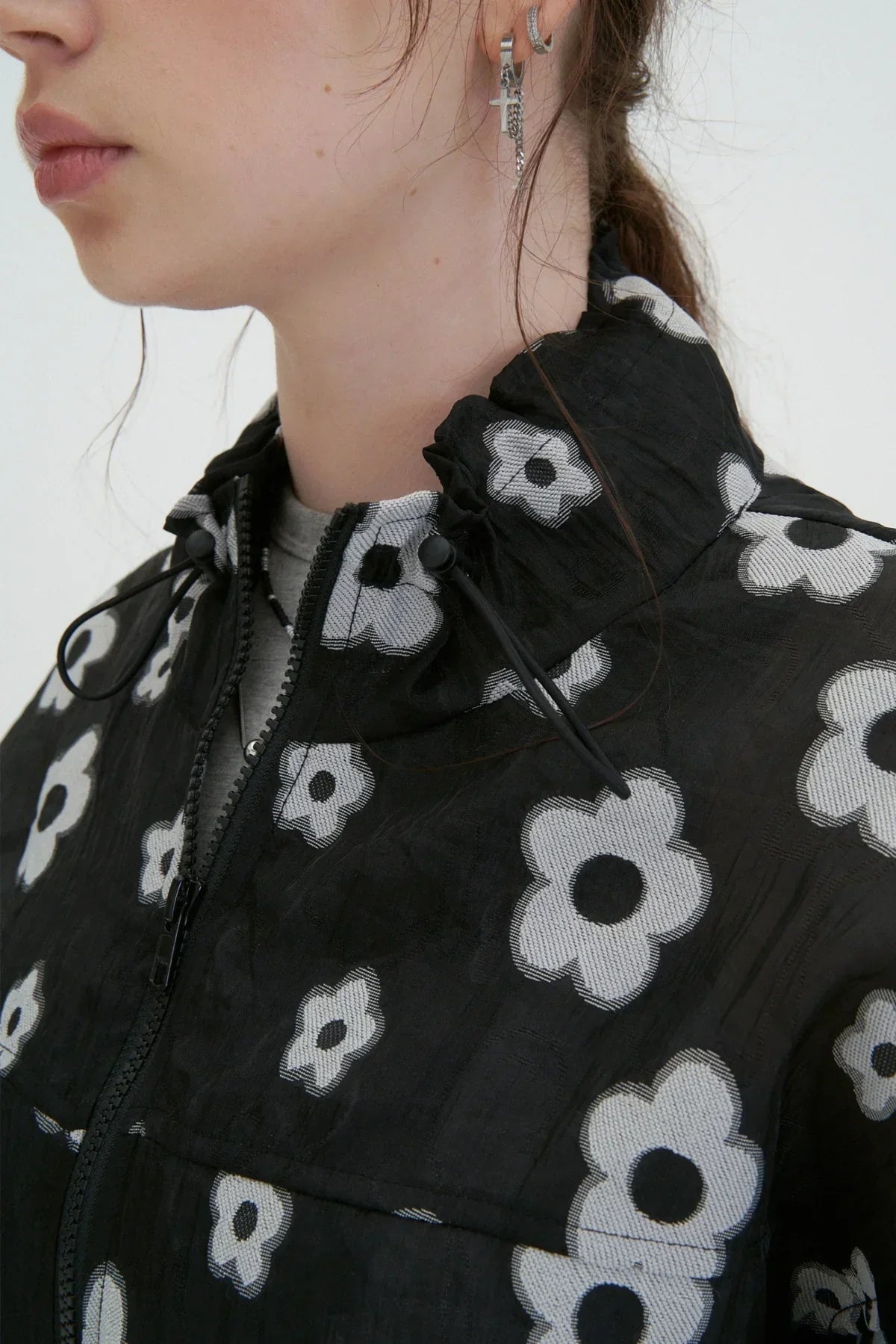 Close-up of woman wearing black zip-up jacket with white flower pattern and silver hoop earrings