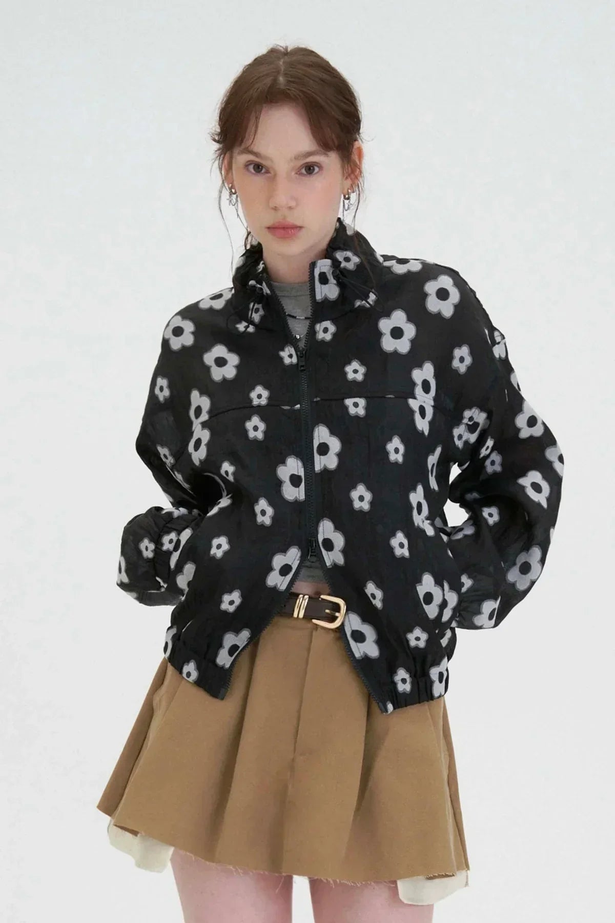 Woman wearing black zip-up jacket with white flower pattern and tan pleated skirt