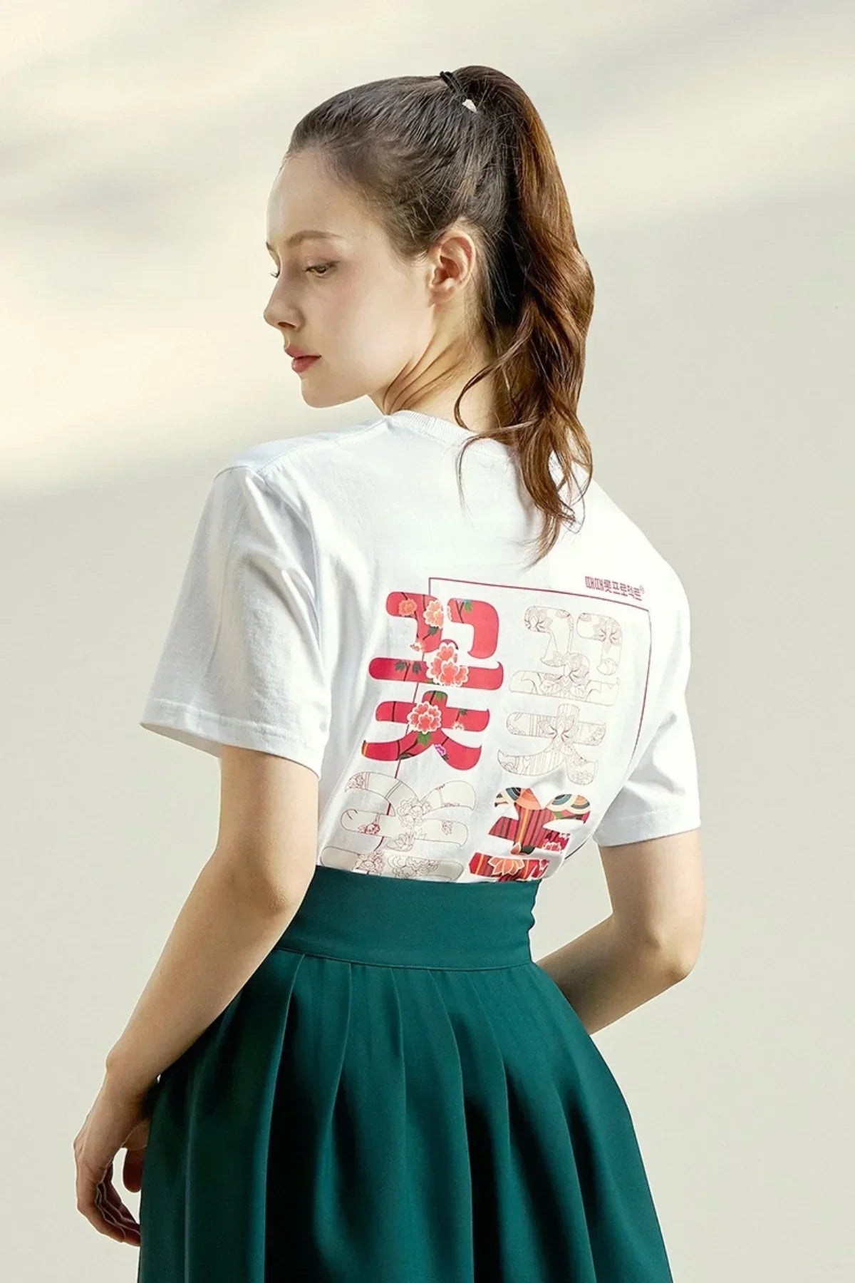 Woman wearing white floral graphic t-shirt with red and pink designs, paired with high-waist green skirt