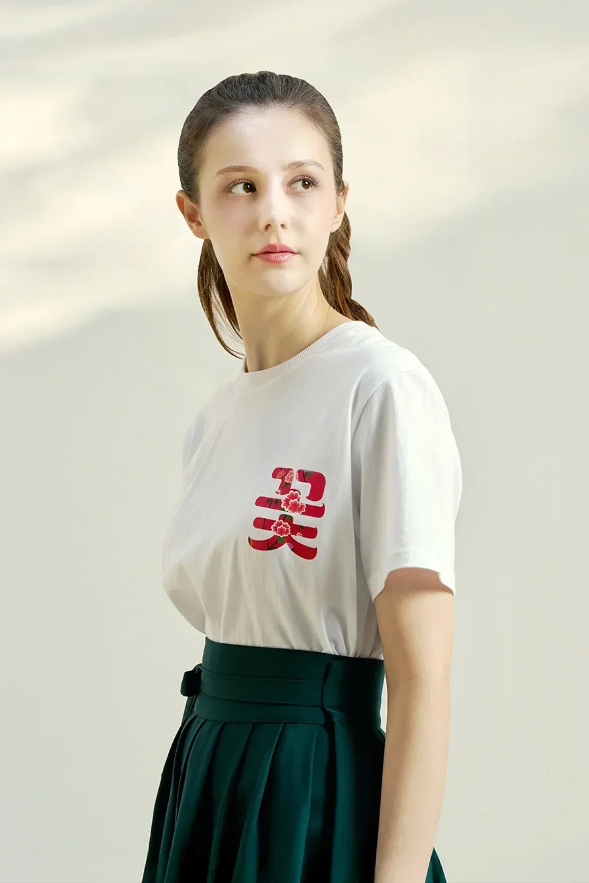 Young woman wearing white t-shirt with red floral Asian character print and dark green high-waisted skirt