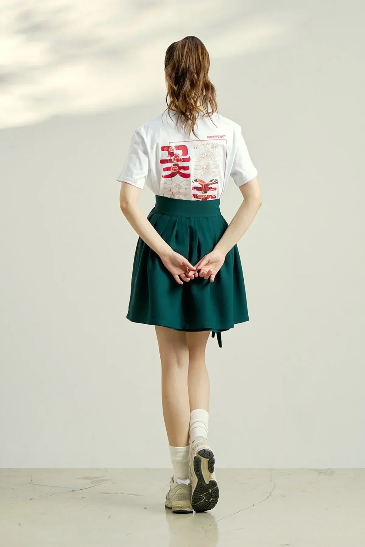 Woman wearing white graphic T-shirt with red floral text and dark green skirt in a studio setting