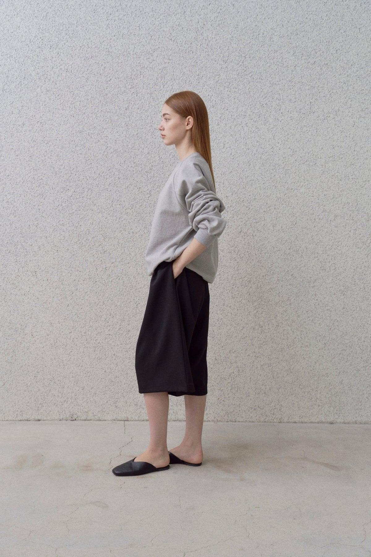 Side view of woman wearing grey round neck sweatshirt with black wide shorts and black slippers