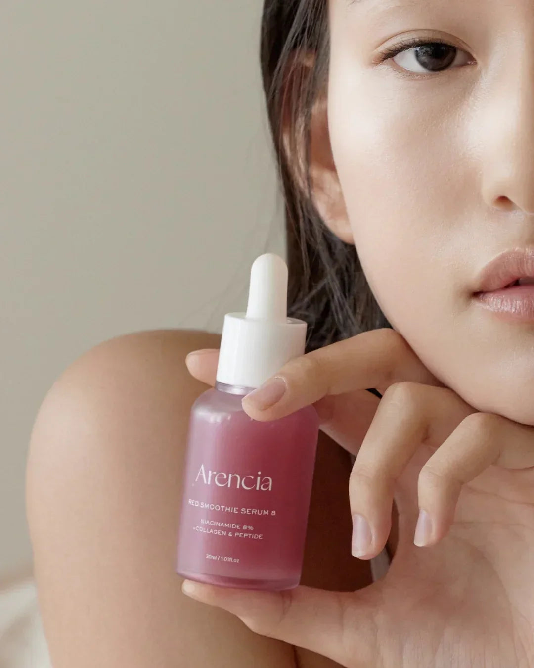 Close-up of a woman holding Arencia Red Smoothie Serum 8 skincare bottle with niacinamide, collagen, and peptide