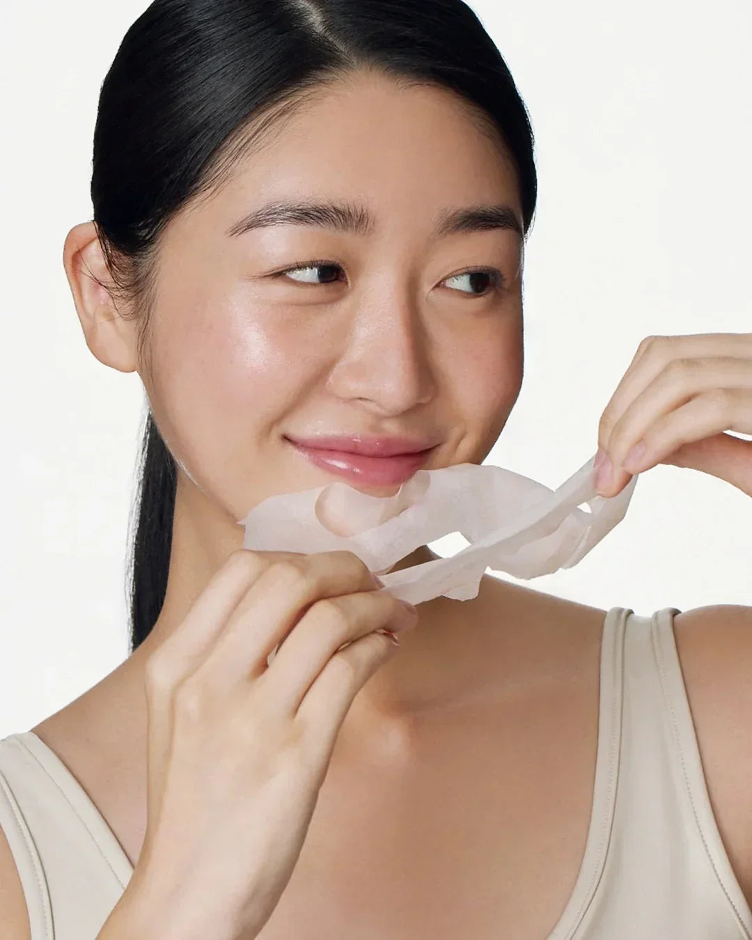 Young woman with glowing skin removing a translucent sheet face mask, skincare beauty routine