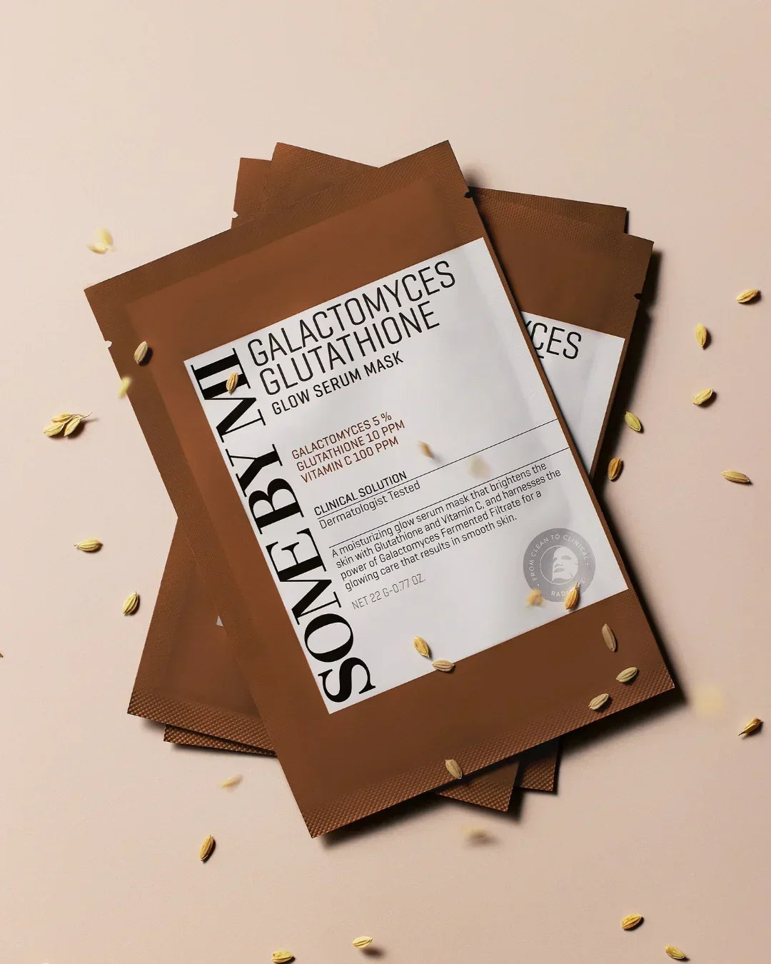 SOME BY MI Galactomyces Glutathione Glow Serum Mask packets on beige background with scattered grains