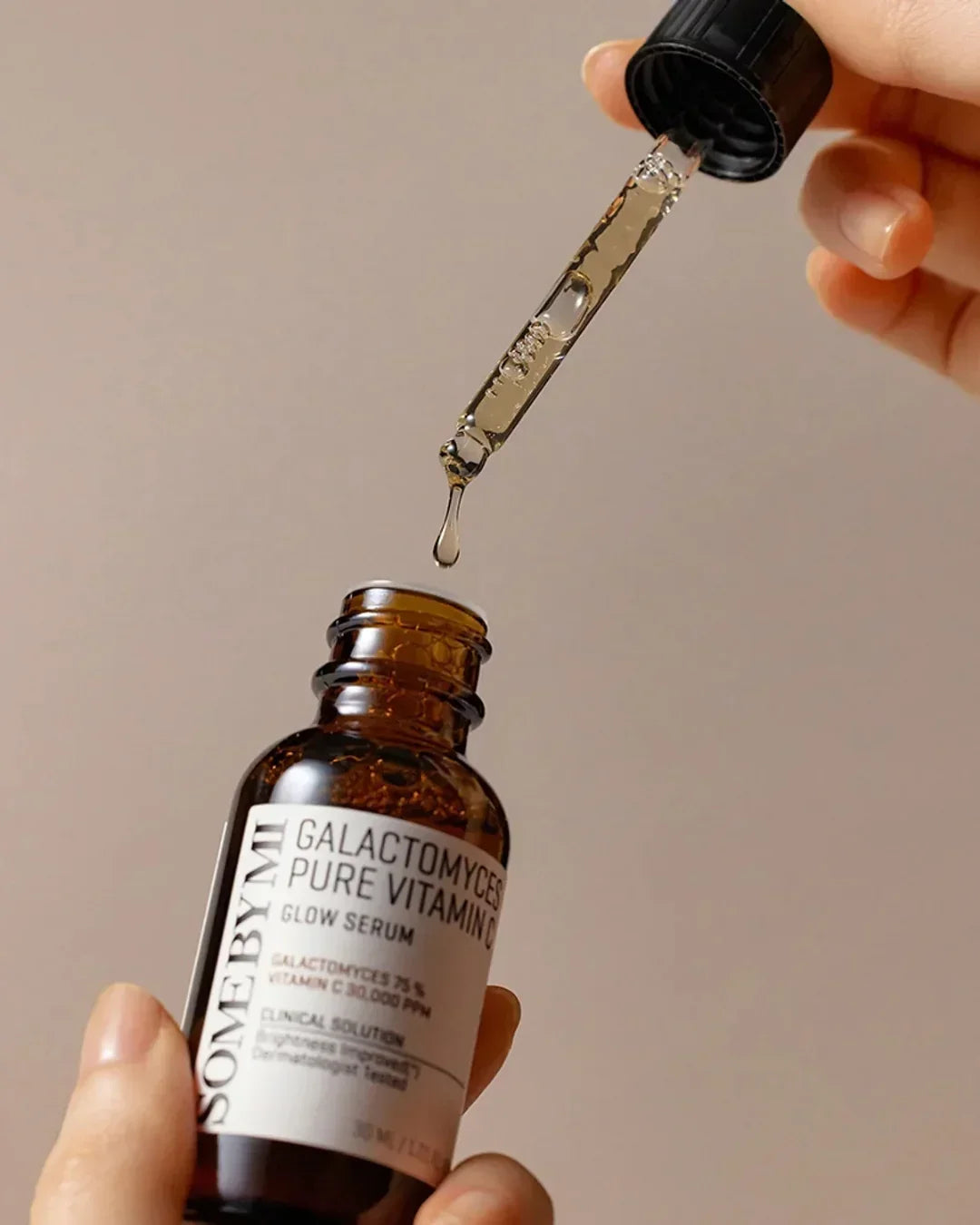 Hand holding Some By Mi Galactomyces Pure Vitamin C Glow Serum bottle with dropper releasing serum drop