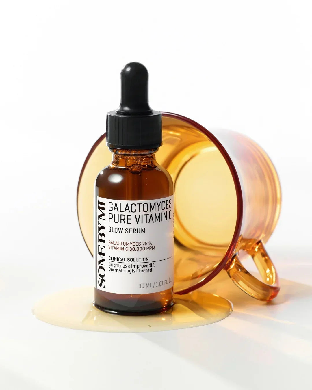 Some By Mi Galactomyces Pure Vitamin C Glow Serum bottle with amber glass cup tipped over on white surface
