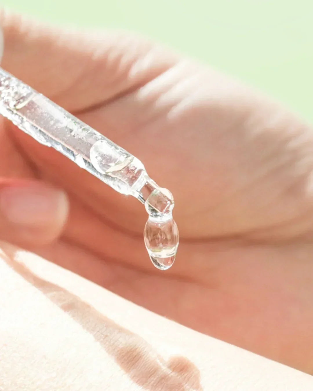Close-up of clear vitamin C serum dropper dispensing liquid serum onto hand skin