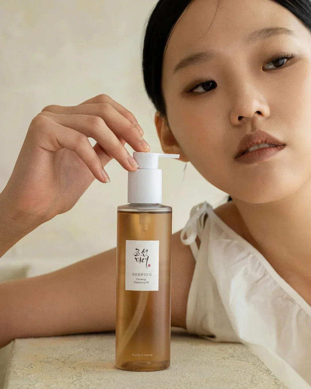 Asian woman in white holding a brown bottle of Ginseng Cleansing Oil with white pump