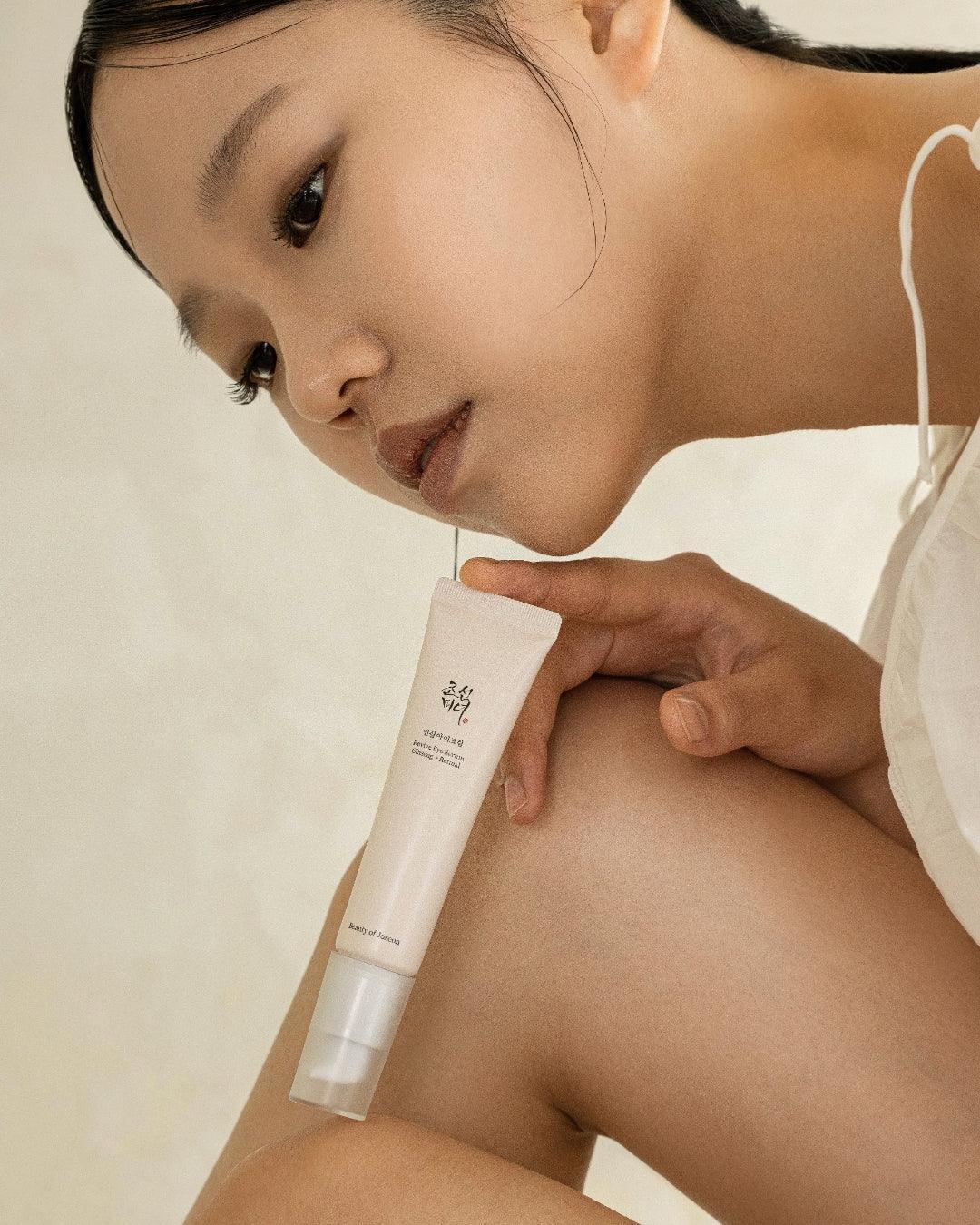 Close-up of woman holding Beauty of Joseon Revive Eye Serum in a minimalist setting