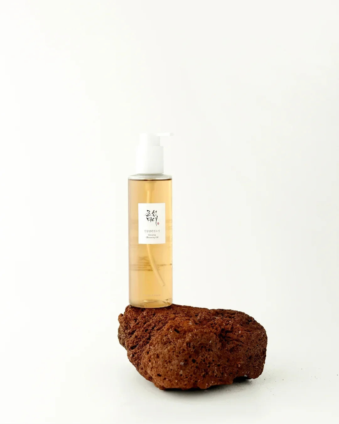 Clear bottle of ginseng cleansing oil with white pump on brown porous stone against white background