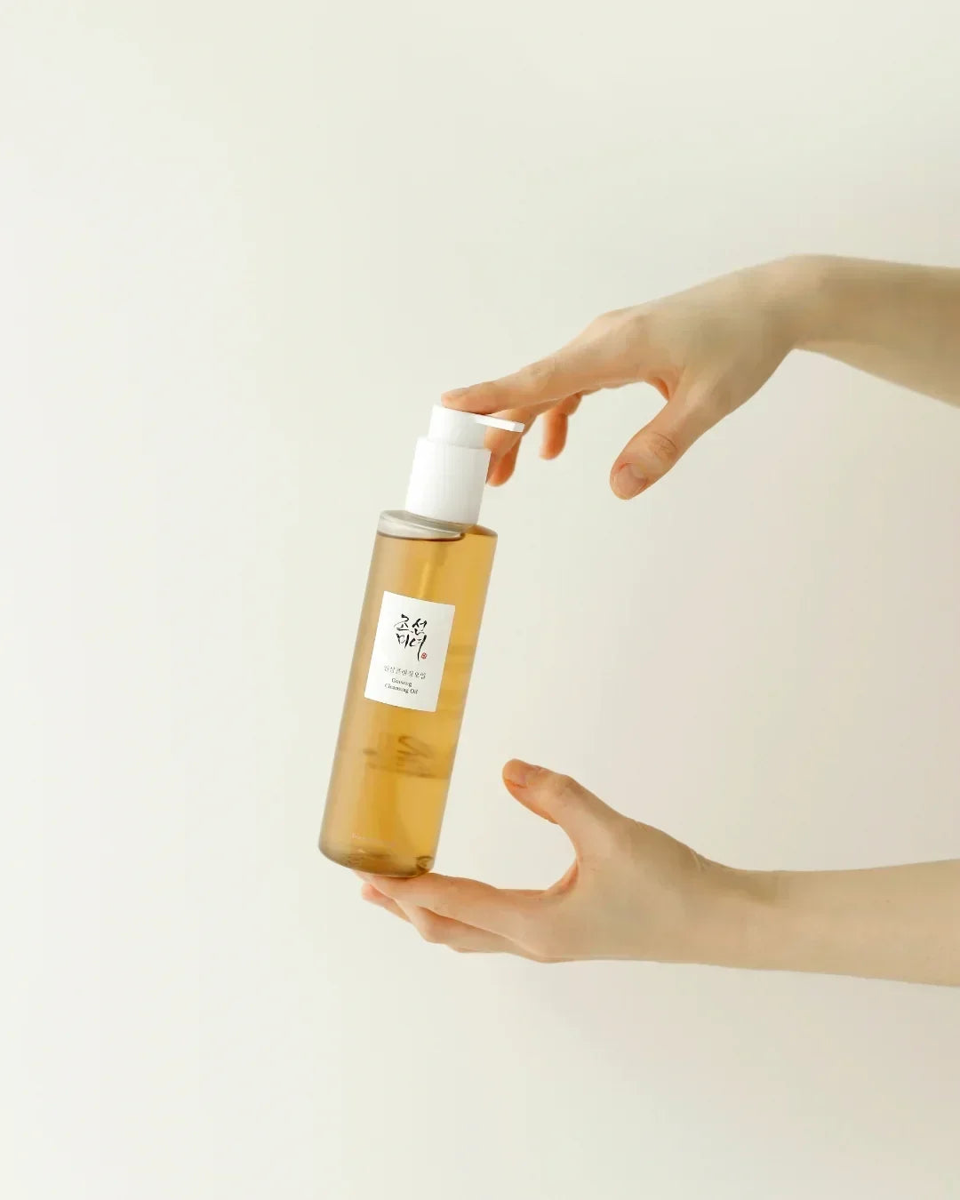 Person holding a bottle of ginseng cleansing oil with white pump against a pale background