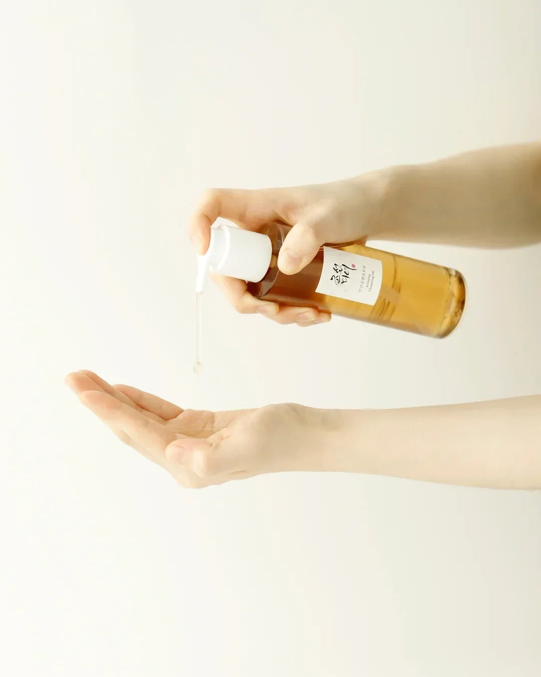 Hand dispensing clear ginseng cleansing oil from amber bottle with white pump onto open palm