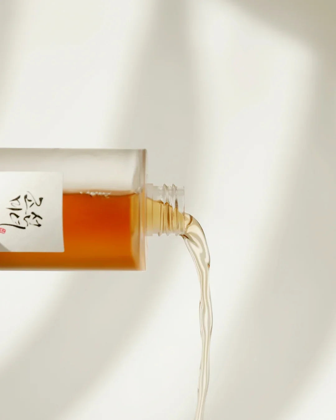 Close-up of ginseng essence water in clear bottle pouring liquid against neutral background