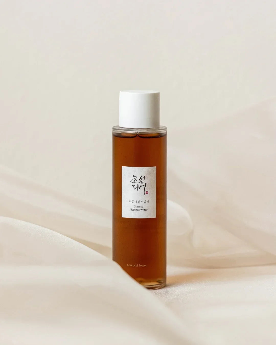 Bottle of Ginseng Essence Water with white cap on soft beige fabric background