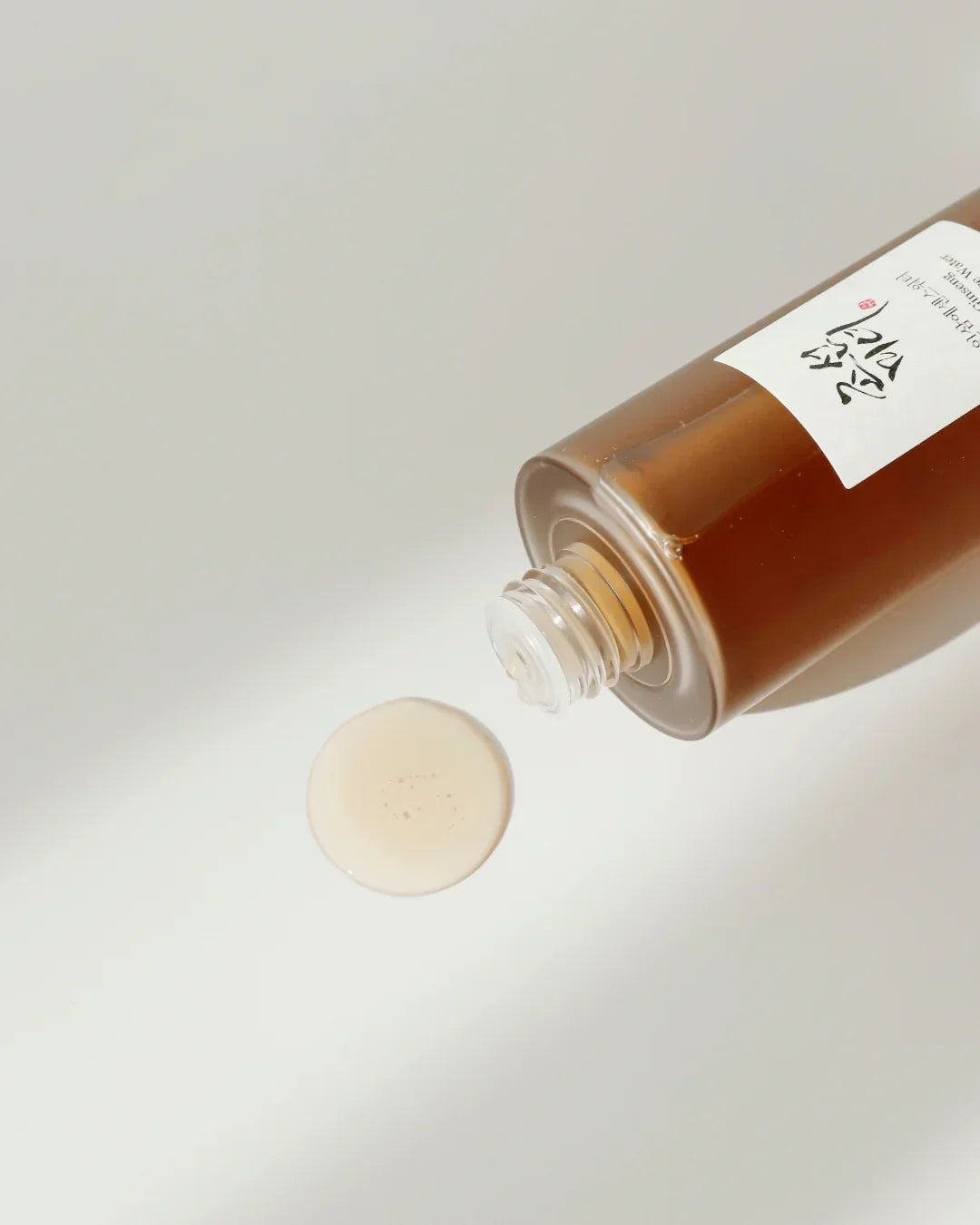Ginseng essence water in a brown bottle with a small spill on a white surface