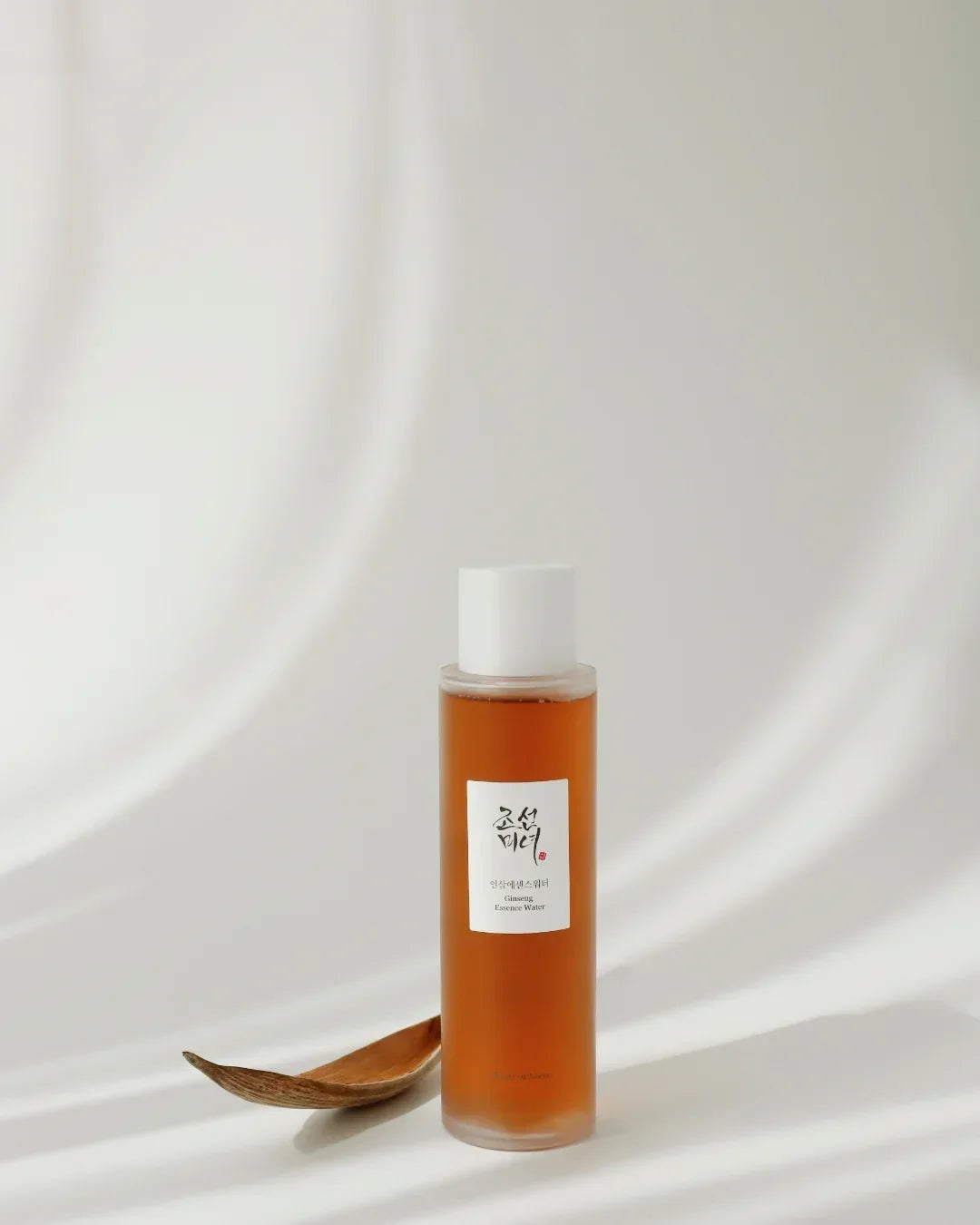 Ginseng Essence Water bottle with white cap on white surface next to wooden spoon