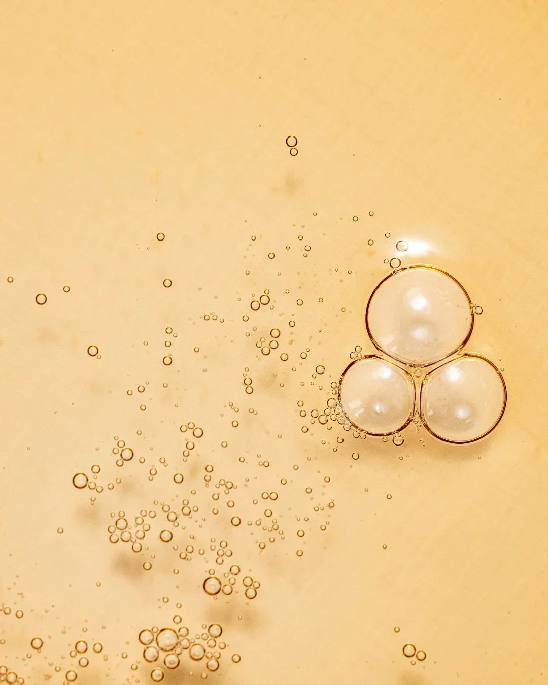 Close-up of golden liquid texture with suspended bubbles and clusters on warm beige background