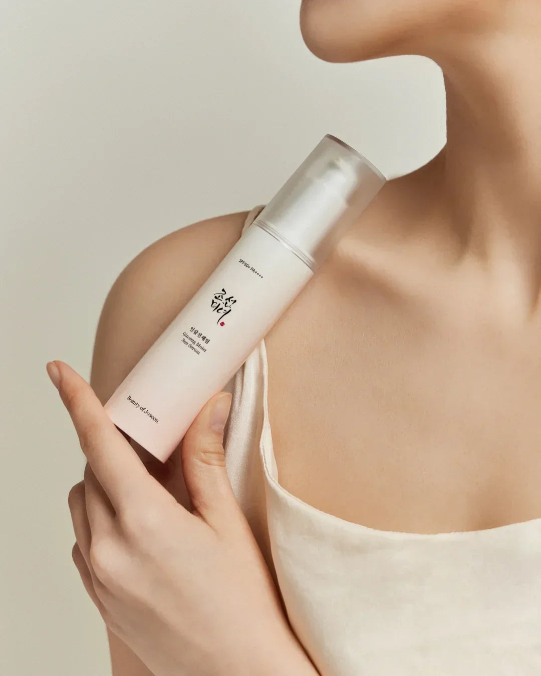 Close-up of a woman holding a Ginseng Moist Sun Serum bottle near her shoulder, showcasing skincare product