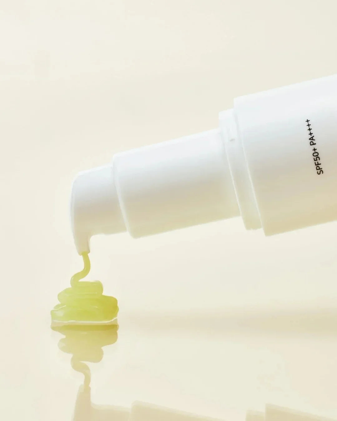 White pump bottle dispensing yellow ginseng sun serum with SPF50+ PA++++ on beige background