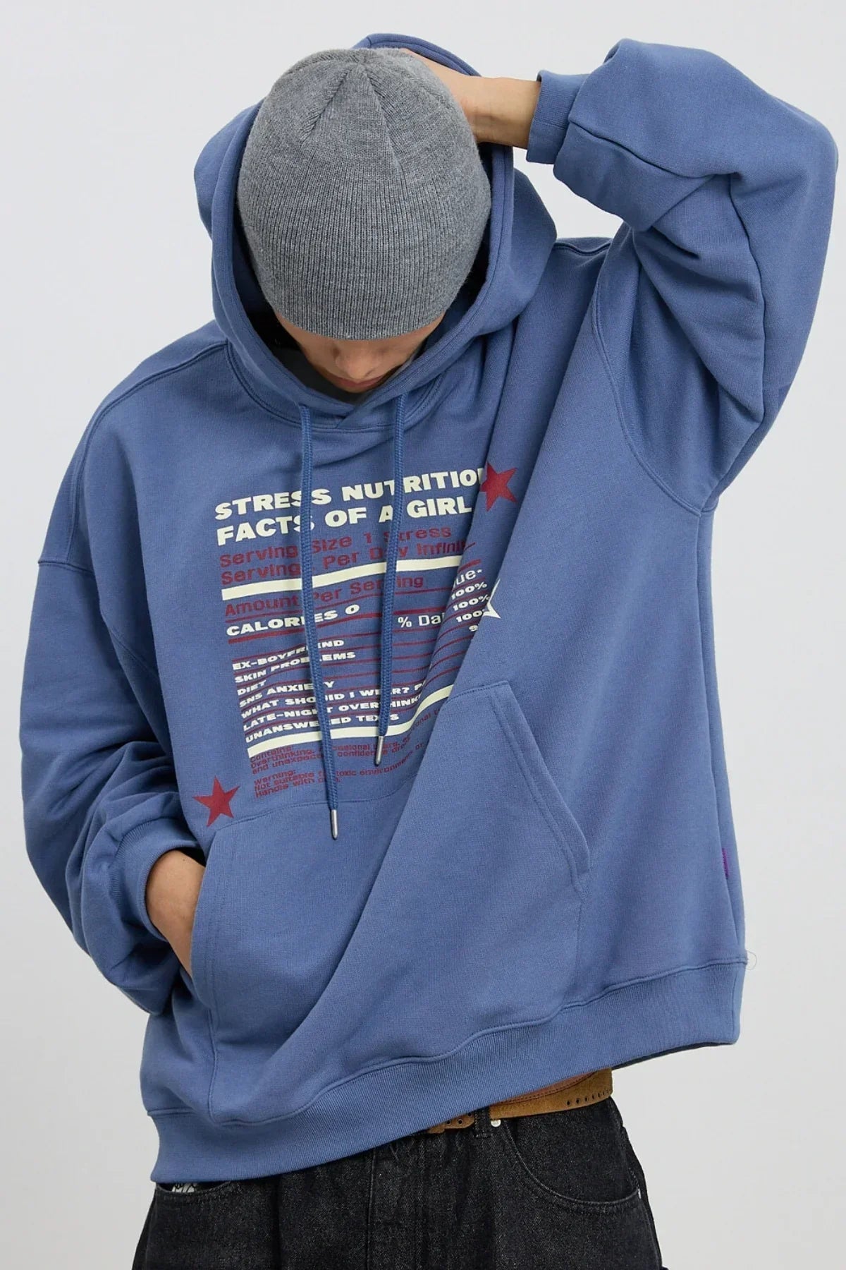 Person wearing dust blue hoodie with stress nutrition facts graphic, grey beanie, hand in pocket