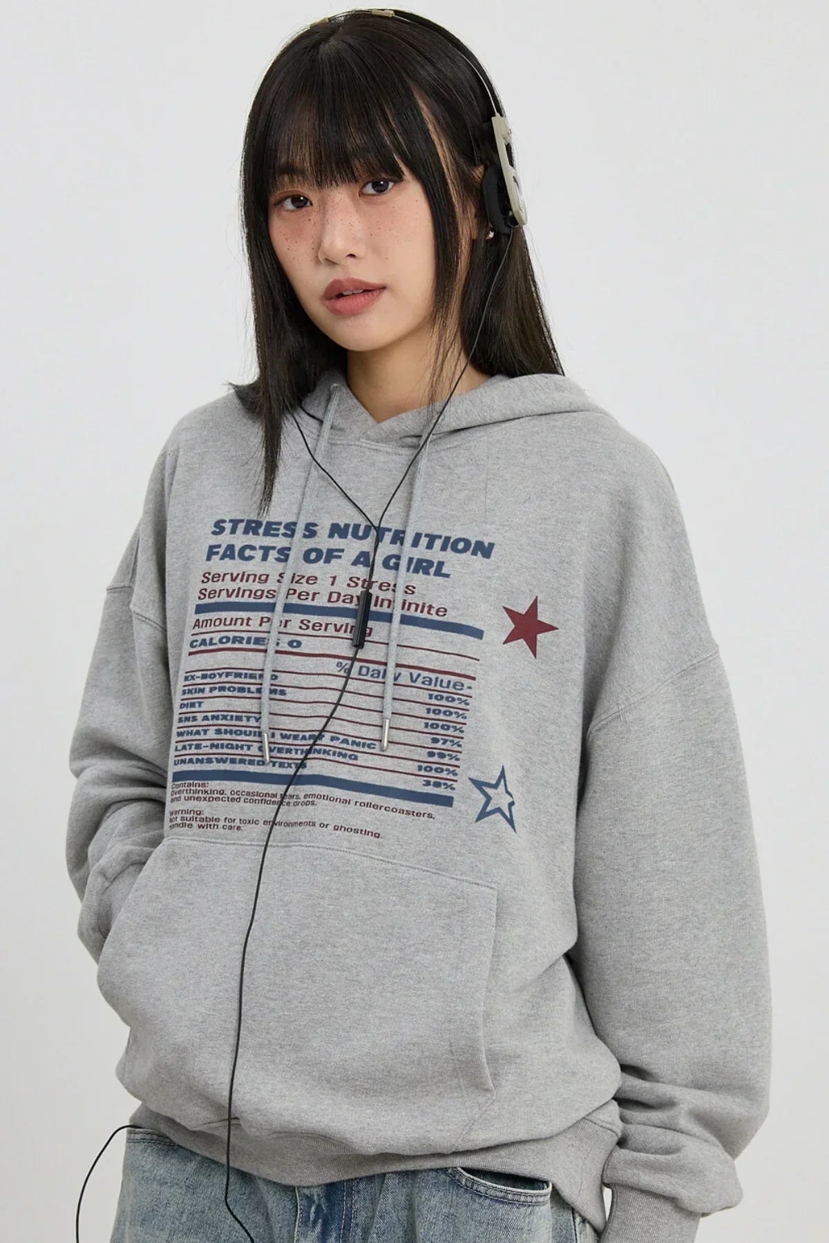 Young woman with straight black hair wearing grey hoodie with stress nutrition print and headphones