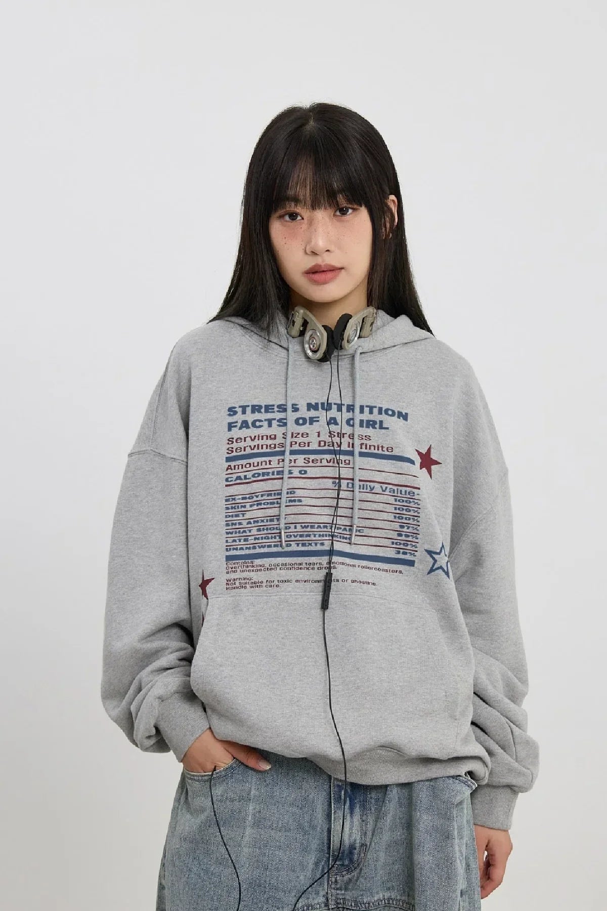 Young woman wearing grey hoodie with printed 'Stress Nutrition Facts of a Girl' text and blue jeans