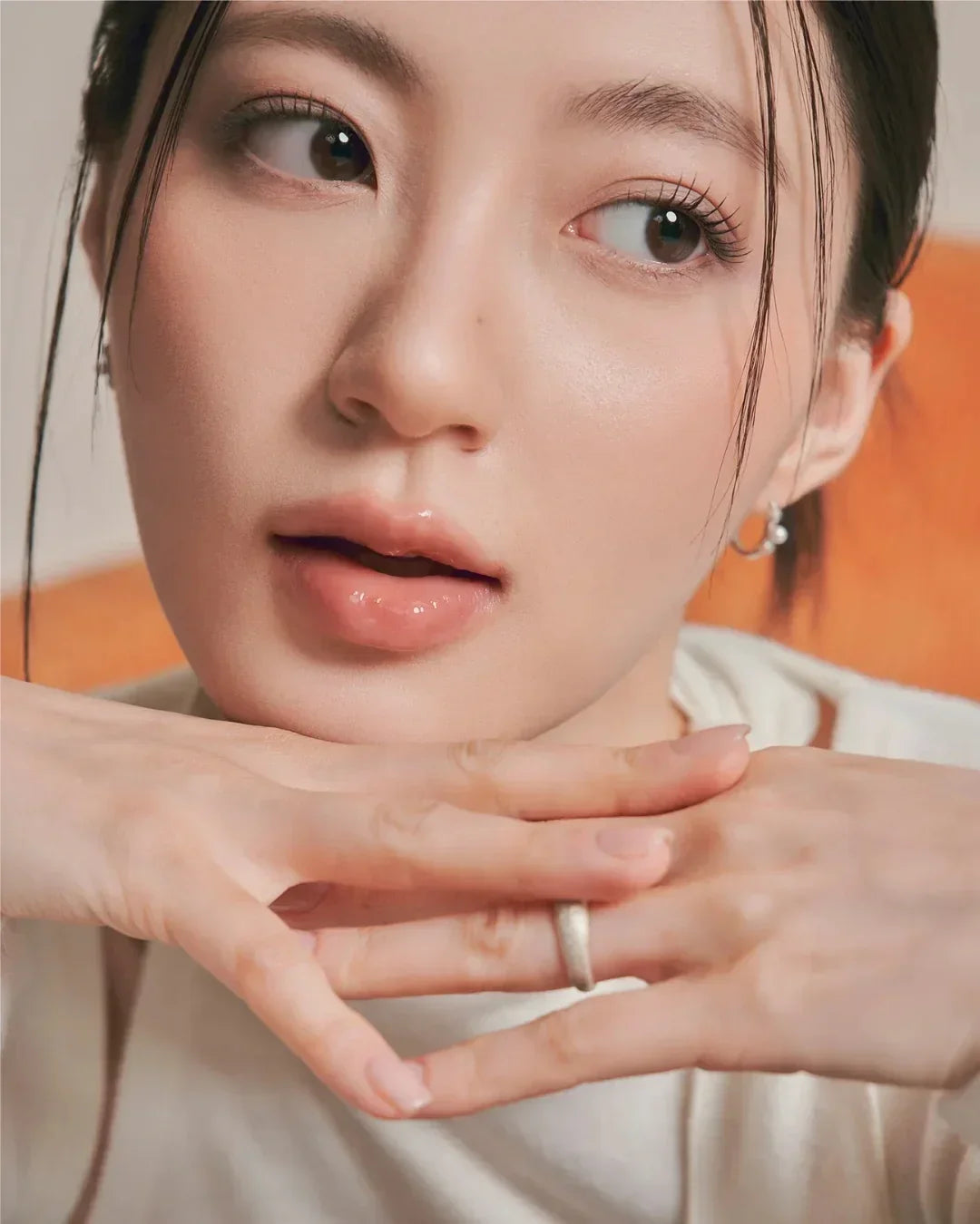 Close-up of woman with glossy lips, natural makeup, and delicate rings, posing with hands near face
