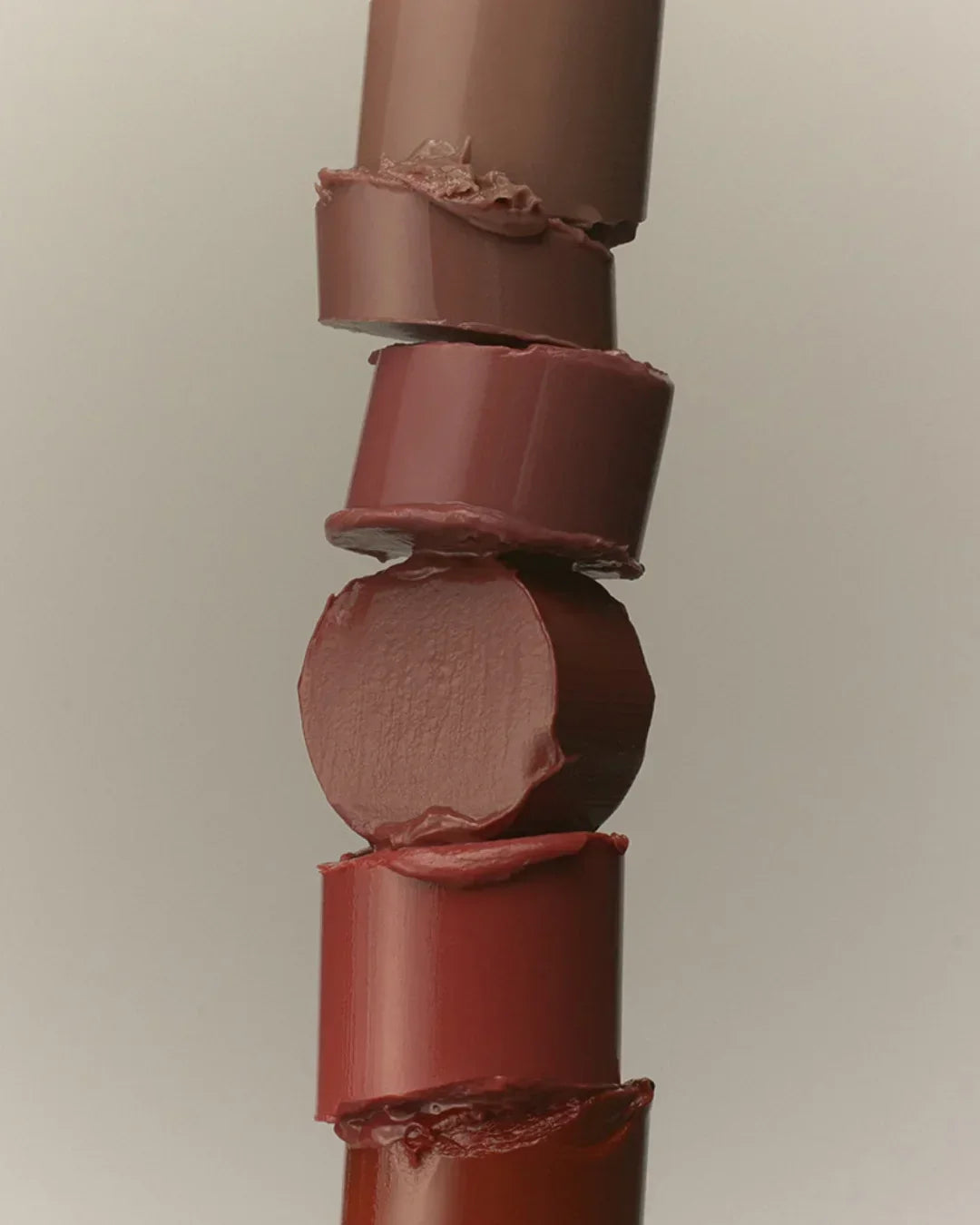 Stack of five cut sections of lipstick in various brown and red shades with creamy texture