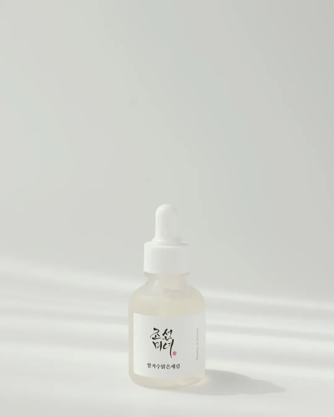 Minimalist dropper bottle serum labeled in Korean on white background with soft shadows