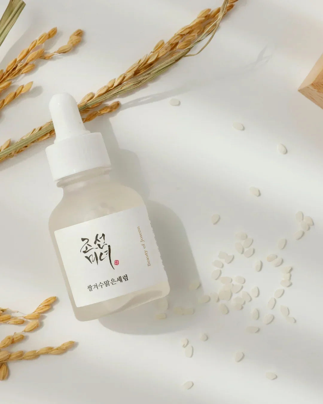 Skincare serum bottle with dropper, rice grains, and dried rice stalks on white background