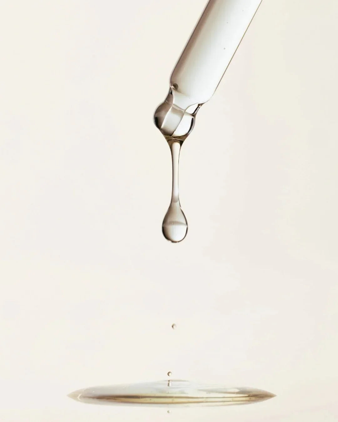 Close-up of clear serum dropping from a glass dropper on a light background
