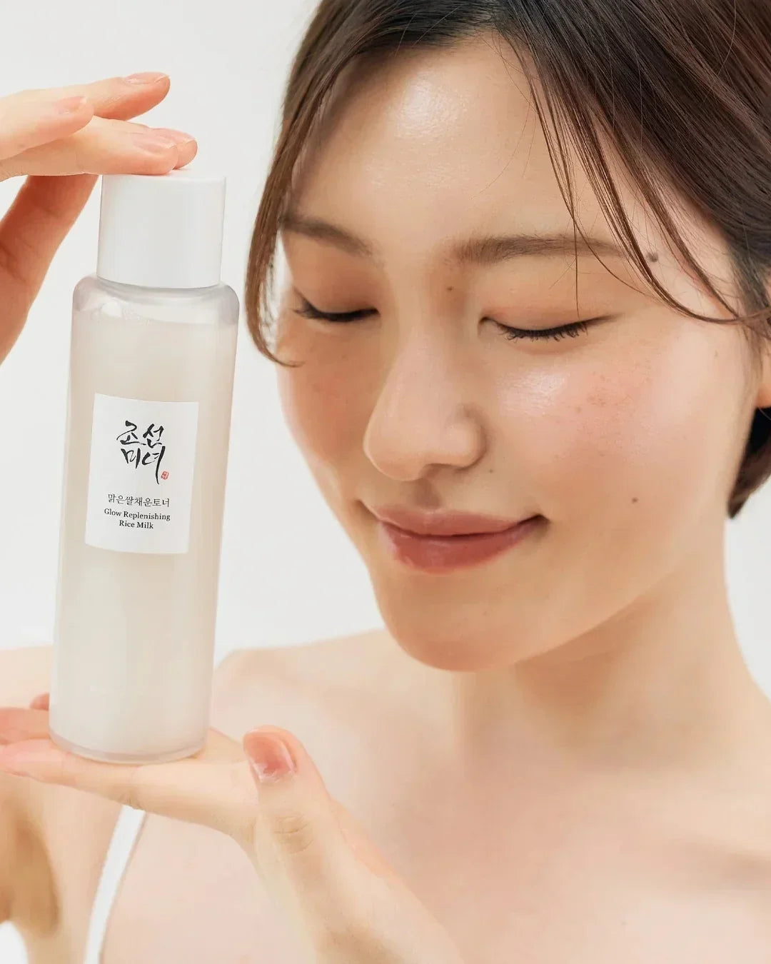 Woman holding Glow Replenishing Rice Milk skincare bottle with clear glowing skin