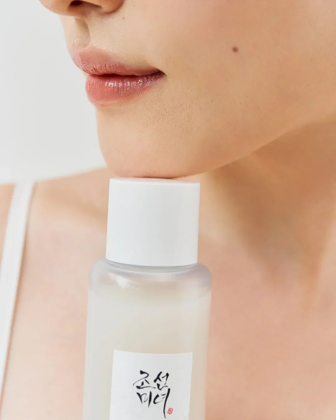 Close-up of woman's lips and chin holding a white-capped bottle with Asian script label