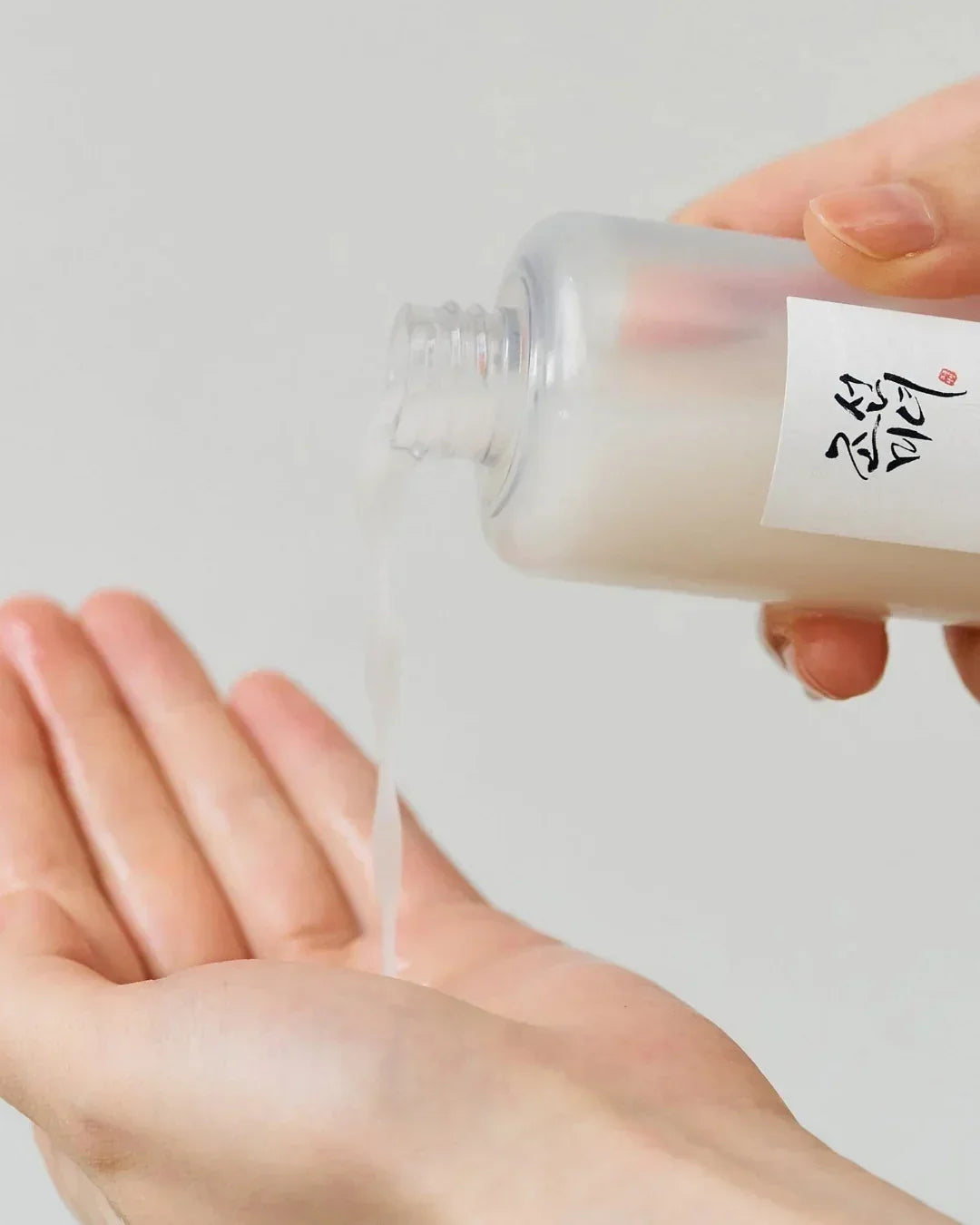 Hand pouring milky skincare serum from frosted bottle with Asian script label into palm