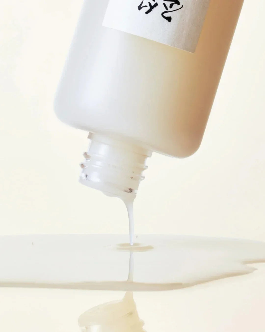 Close-up of white bottle pouring milky liquid onto reflective surface with Asian characters on label