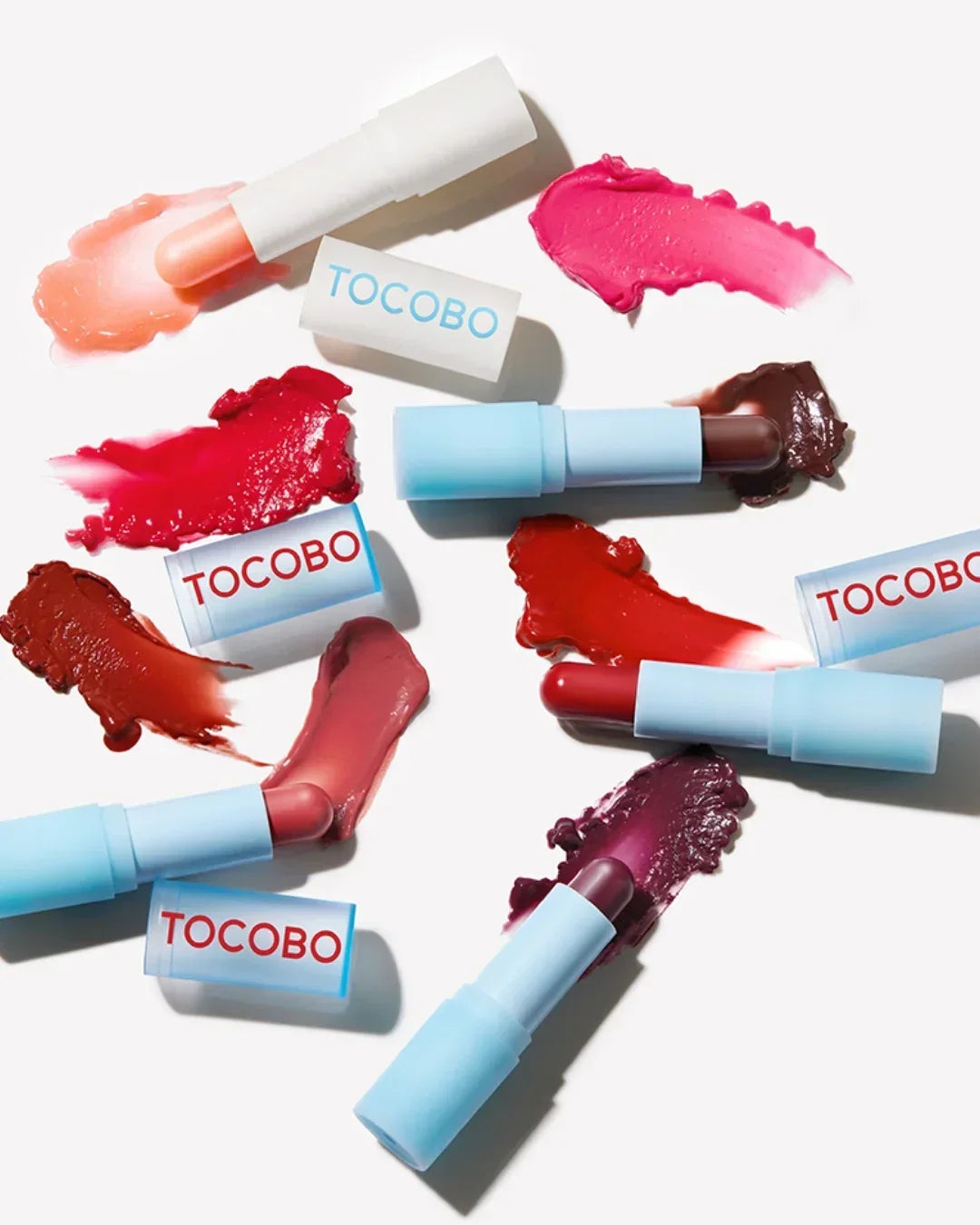 Tocobo lip balms with light blue tubes and various bold lipstick shades swatched on white background