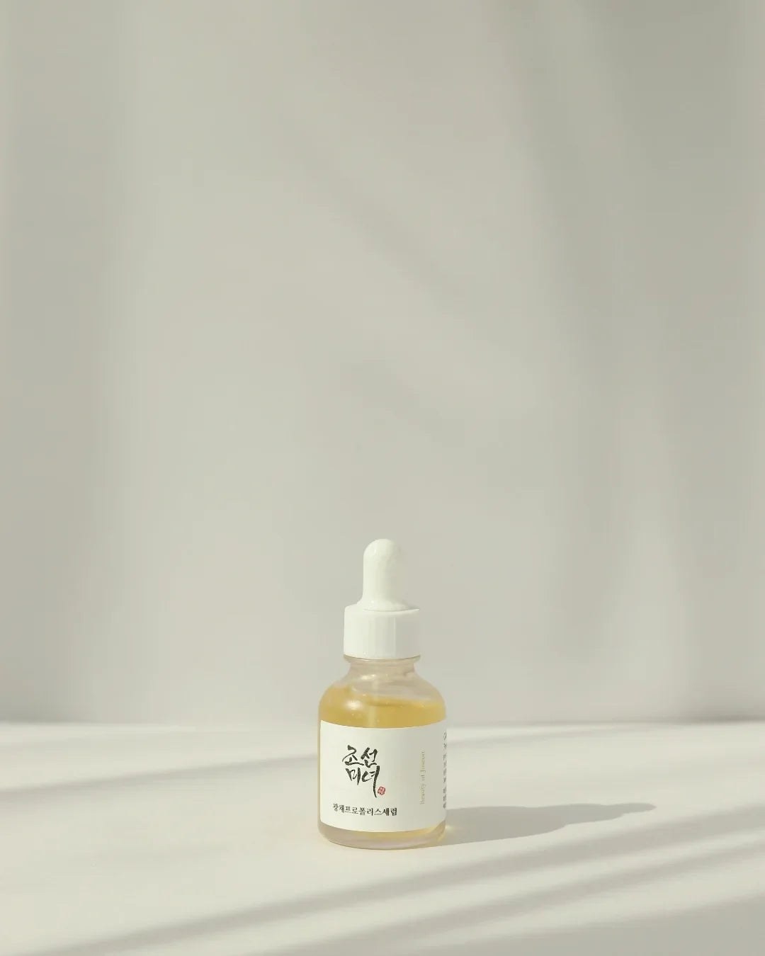 Dropper bottle of Korean skincare glow serum with propolis and niacinamide on white surface